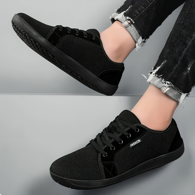 Sort minimalistisk barfodssko set fra siden og ovenfra, båret sammen med sorte jeans
