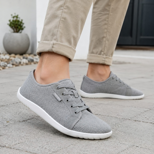 Grå barfodssko til både mænd og kvinder, båret udendørs på en stenbelagt overflade sammen med beige chinos