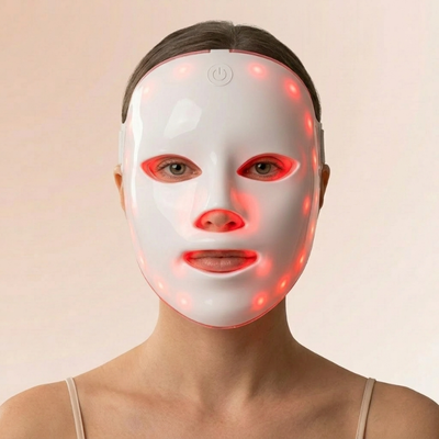 Kvinde med en hvid InfraRelief™ LED-ansigtsmaske med rødt lys, set forfra på en beige baggrund