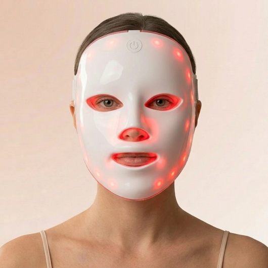 Kvinde med en hvid InfraRelief™ LED-ansigtsmaske med rødt lys, set forfra på en beige baggrund