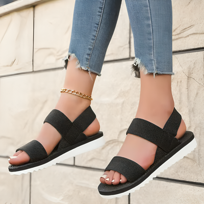 Sort: Elastiske mesh-sandaler med dobbelte remme i sort – Dame, set nedenfra med murstensbaggrund
