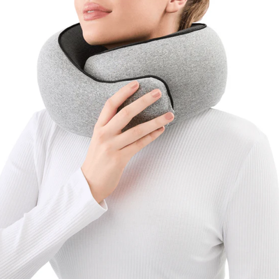 En kvinde har en grå rejsepude om halsen og justerer pasformen med den ene hånd; her ses den ergonomiske nakkestøtte set forfra